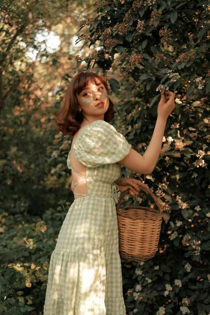 A woman in a vintage dress gracefully picks flowers in a sunlit garden, exuding classic beauty.